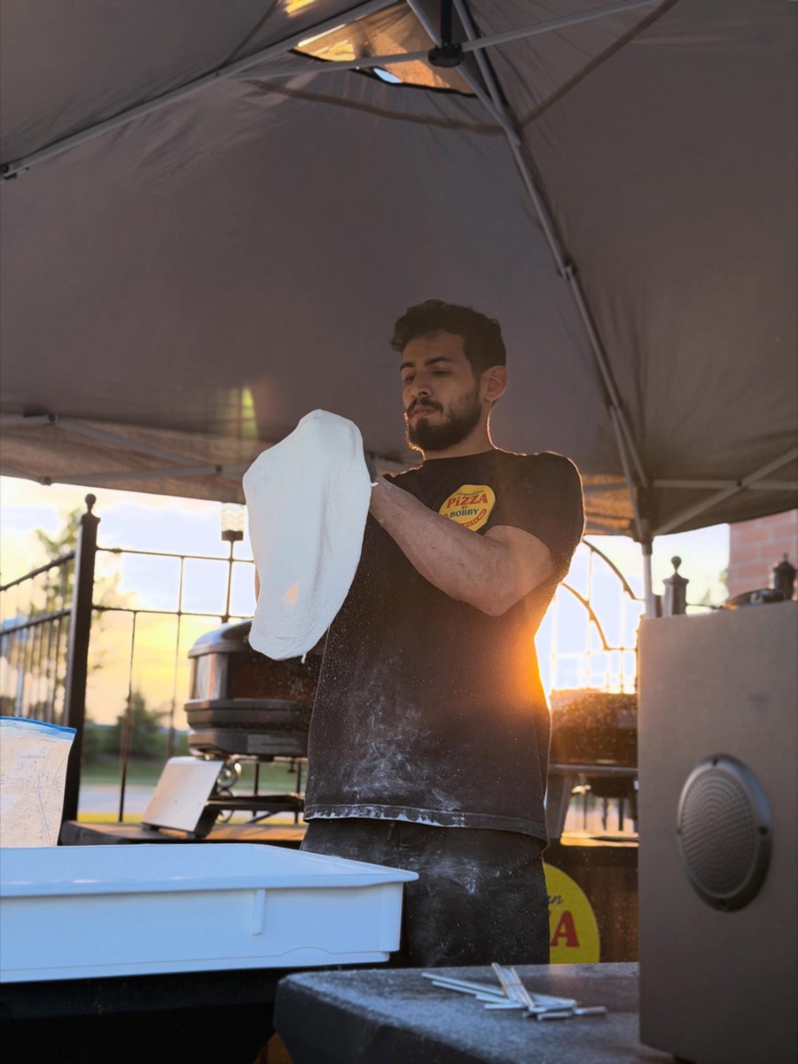 Bobby hand-stretching pizza dough at golden hour under the event tent