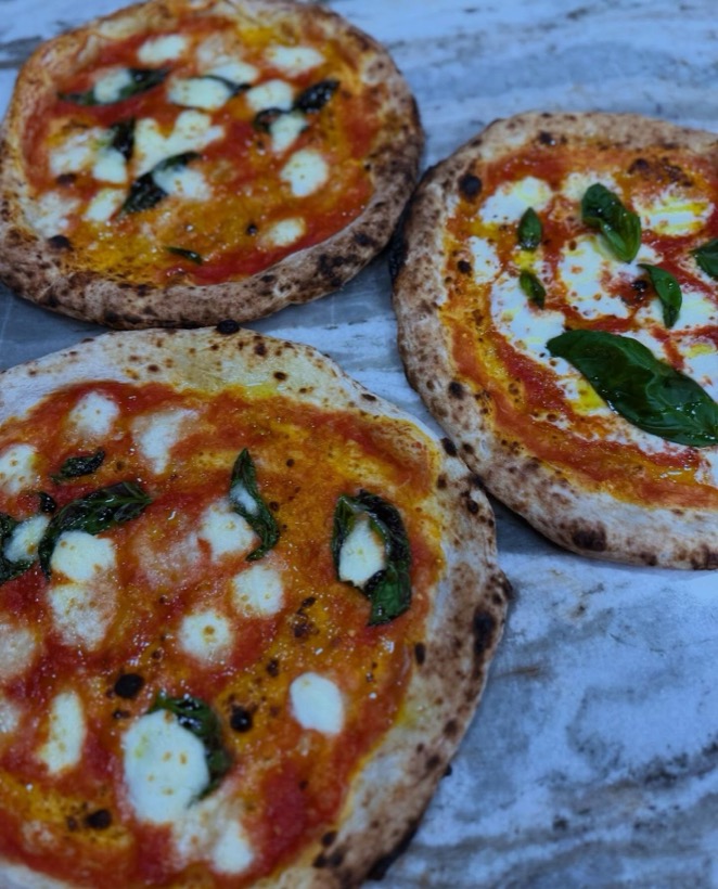 Three Neapolitan margherita pizzas on a marble counter